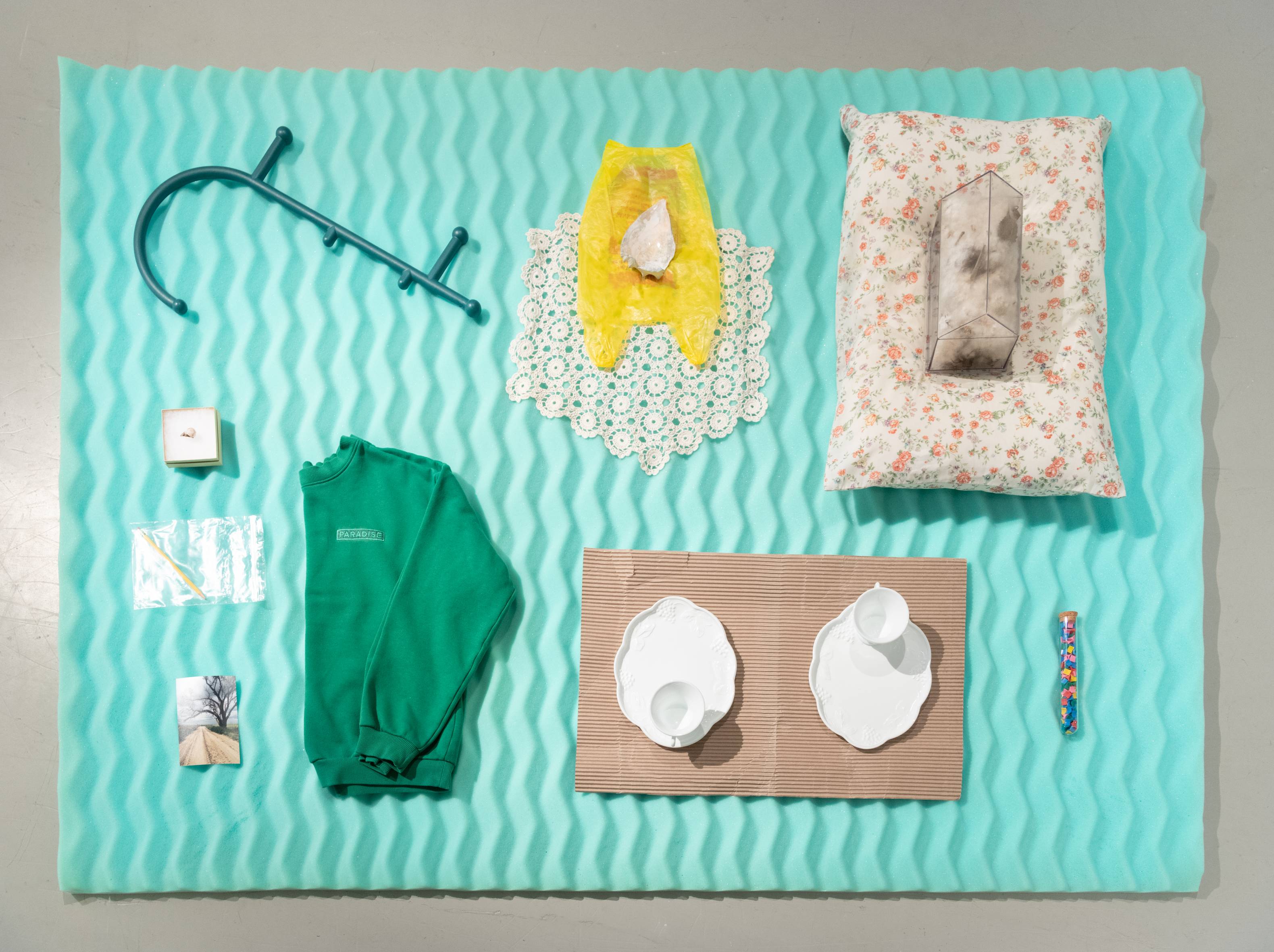 Overhead view of floor sculpture with various objects on top such as a green sweatshirt and a pillow 